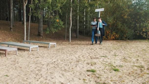 Dos hombres con letrero de la ciudad caminando en la playa de arena mirando en la tableta monitor — Vídeos de Stock