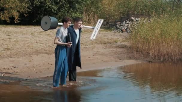 Two guys stand in water shore looking down, talking and start shout summer day — Stock Video