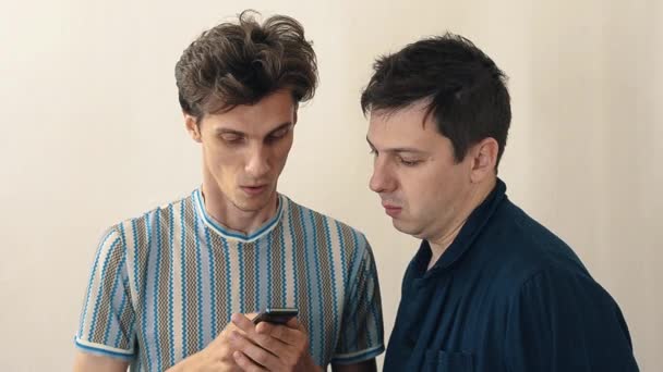 Dos hombres entusiastas de pie en la sala blanca con teléfono celular — Vídeo de stock