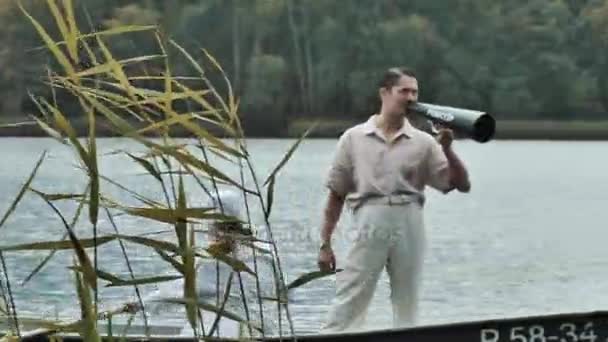 Медсестра катается на лодке по озеру, мужчина в сетке для волос кричит в мегафон — стоковое видео