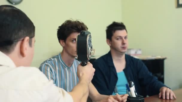 Человек в сетке для волос использовать ретро 8 мм камера в офисе расстрел двух рабочих — стоковое видео