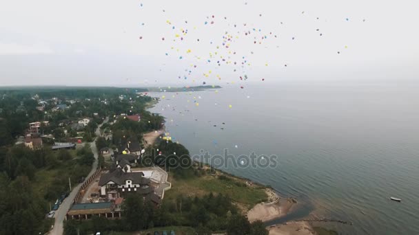 Aerial shot lots of colorful balloons flying up in to sky over sea shore beach — Stock Video