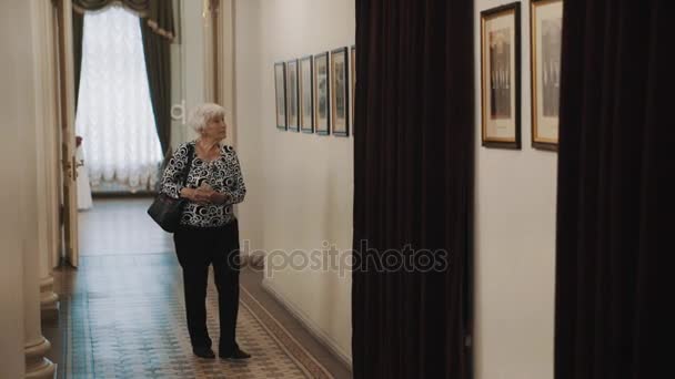 Sankt Petersburg, Ryssland - 23 juni 2016: gammal kvinna iakttar bilder på väggen i korridoren i gammal klassisk stil inredning — Stockvideo