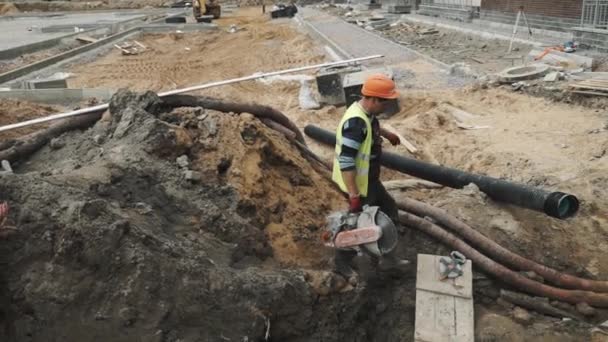 Sankt Petersburg, Ryssland - 26 September 2016: Slowmotion arbetare i orange hård hatt promenad cirkelsåg i diket på byggnadsplatsen — Stockvideo
