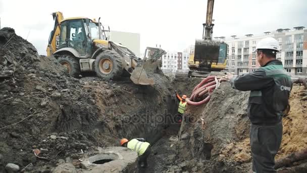 SAN PETERSBURG, RUSIA - 26 DE SEPTIEMBRE DE 2016: Los trabajadores de cámara lenta hacen gestos al conductor de la excavadora arrojando piedras en la zanja — Vídeo de stock