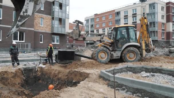 SAINT PETERSBURG, RUSSIA - SEPTEMBER 26, 2016: Slowmotion worker lowering concrete manhole ring swinging on bulldozer ladle — Stock Video