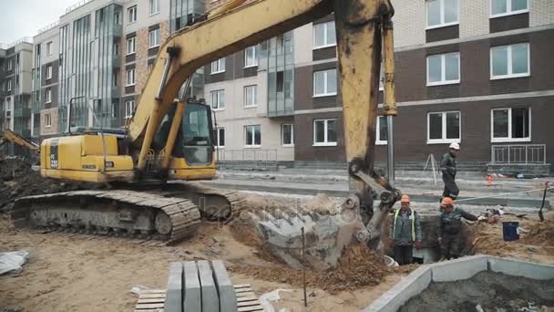 SAN PETERSBURG, RUSIA - 26 DE SEPTIEMBRE DE 2016: La excavadora amarilla de cámara lenta lanza anillos de alcantarillado de hormigón de arena en zanja — Vídeo de stock