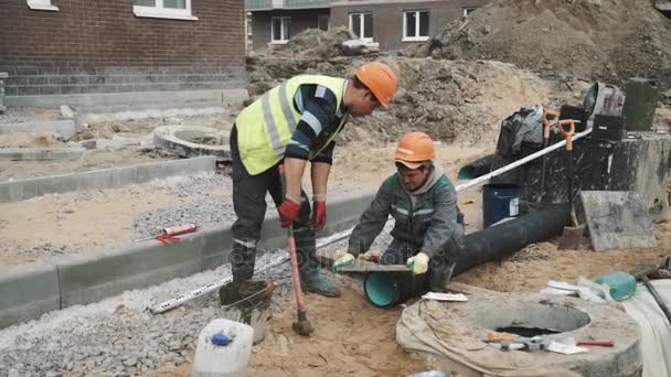 Sint-Petersburg, Rusland - 26 September 2016: Werknemer in harde hoed raken stuk hout op zwarte plastic pijp op de bouwplaats — Stockvideo