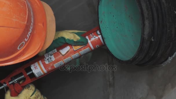 SAINT PETERSBURG, RUSSIA - 26 SETTEMBRE 2016: Lavoratore da vicino in berretto rigido uso sigillante su tubo di plastica colorato in calcestruzzo — Video Stock