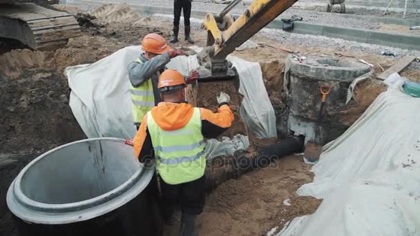 Sankt Petersburg, Ryssland - 26 September 2016: Arbetstagare i hårda hattar leder grävmaskin dumpning sand på plaströr i dike — Stockvideo