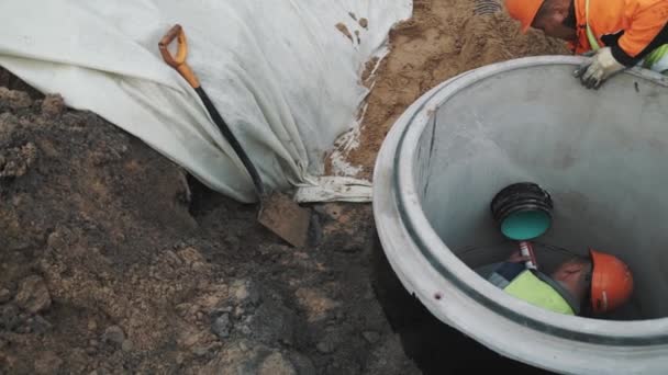 SAINT PETERSBURG, RUSSIA - 26 СЕНТЯБРЯ 2016: Builder in hard hat inside concrete manhole ring using sealant on plastic tube — стоковое видео