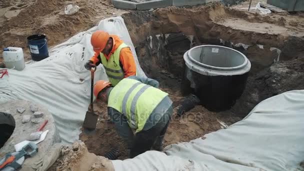 SAINT PETERSBURG, RÚSSIA - 26 de setembro de 2016: Trabalhadores em chapéus duros com pás cavando areia em vala de esgoto no canteiro de obras — Vídeo de Stock