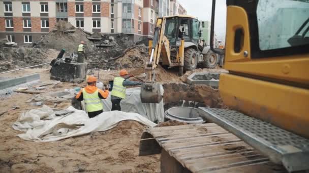 Sankt Petersburg, Ryssland - 26 September 2016: Byggare s i hårda hattar leder grävmaskin dumpning sand i avlopp dike vit tyg — Stockvideo