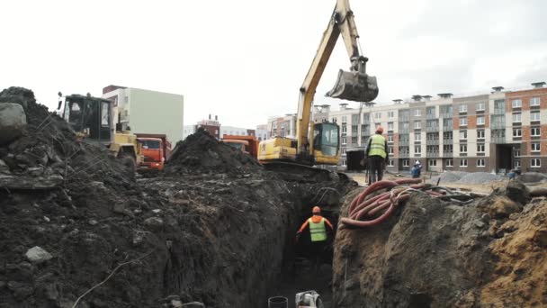 SAN PETERSBURG, RUSIA - 26 DE SEPTIEMBRE DE 2016: Trabajador con sombrero duro arranca anillo de alcantarilla de cámara de hormigón del cucharón de la excavadora — Vídeos de Stock