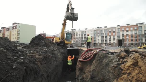 SAN PETERSBURG, RUSIA - 26 DE SEPTIEMBRE DE 2016: Constructores bajan el anillo de alcantarilla de hormigón del cucharón de la excavadora por la zanja — Vídeos de Stock