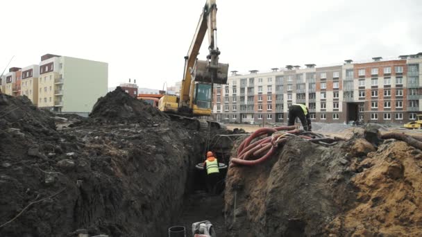 SAN PETERSBURG, RUSIA - 26 DE SEPTIEMBRE DE 2016: Constructores bajan el anillo de alcantarilla de hormigón del cucharón de la excavadora por la zanja — Vídeos de Stock