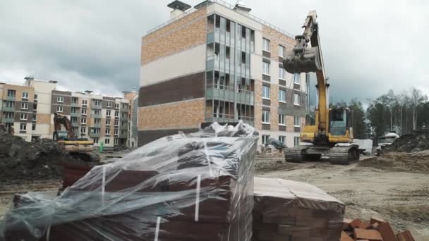 Sint-Petersburg, Rusland - 26 September 2016: Gele graafmachine draagt op kettingen concrete mangat ring op de bouwplaats. — Stockvideo