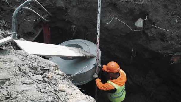 SAN PETERSBURG, RUSIA - 26 DE SEPTIEMBRE DE 2016: Trabajador en casco duro mide anillo de alcantarilla de cámara de hormigón en obra — Vídeos de Stock