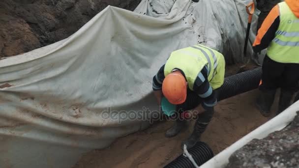 SAINT PETERSBURG, RUSSIE - 26 SEPTEMBRE 2016 : Un travailleur en casque rigide tient un long tuyau en plastique entre les jambes dans un fossé sur le chantier — Video