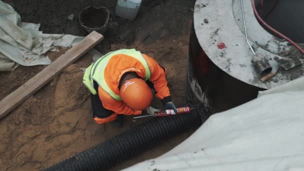 俄罗斯圣彼得堡-2016 年 9 月 26 日︰ 工人的安全帽使用密封胶对塑料管材在混凝土检查井环沟 — 图库视频影像