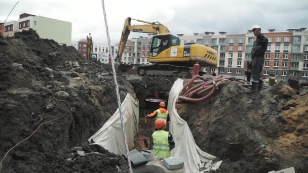 SAN PETERSBURG, RUSIA - 26 DE SEPTIEMBRE DE 2016: Excavadora en obra arroja arena para zanja con dos trabajadores en sombreros duros — Vídeos de Stock