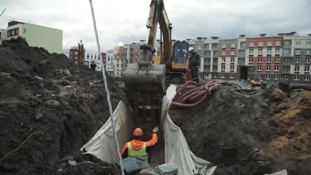 SAN PETERSBURG, RUSIA - 26 DE SEPTIEMBRE DE 2016: Excavadora en obra arroja tierra para zanja con trabajador en sombreros duros — Vídeos de Stock