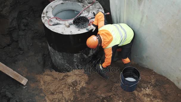 SAN PETERSBURG, RUSIA - 26 DE SEPTIEMBRE DE 2016: Trabajador en casco duro aplicando alquitrán sobre tubo de plástico en anillo de alcantarilla de cámara de hormigón — Vídeos de Stock