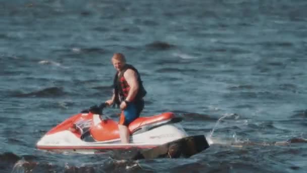 SAINT PETERSBURG, RUSSIA - AUGUST 28, 2016: Man in black vest on a jet ski accurately passing by surfer who floats in water — Stock Video