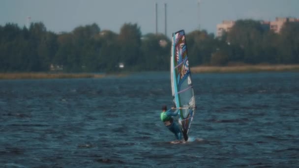 SAN PETERSBURG, RUSIA - 28 DE AGOSTO DE 2016: El hombre de traje de baño azul completo monta windsurf en el lago con edificios en el fondo — Vídeo de stock