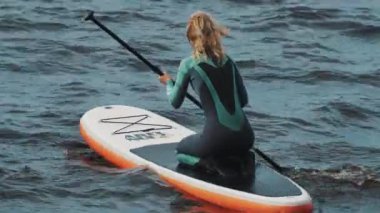 Saint Petersburg, Rusya Federasyonu - 28 Ağustos 2016: ihtimal sportswomen tam mayo oturuşta, bir sörf tahtası raket kullanarak sürmek