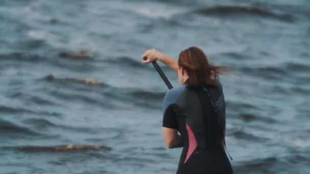 SAINT PETERSBURG, RÚSSIA - 28 de agosto de 2016: Medium shot of sportswoman in full swimsuit rides a surfboard using paddle — Vídeo de Stock