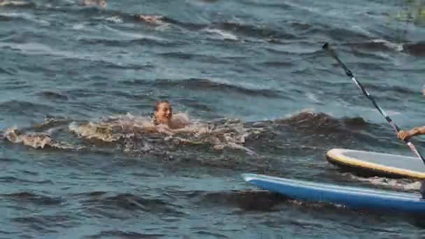 САЙНТ-ПЕТЕРБУРГ, РОССИЯ - 28 августа 2016 года: Молодые женщины в купальниках падают с доски для серфинга в воду, смеются и валяют дурака — стоковое видео