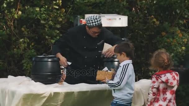 SAINT PETERSBURG, RUSSIE - 28 AOÛT 2016 : Chef cuisinier assemble des chaudières à l'extérieur sur une table de pique-nique. Les enfants errent autour — Video
