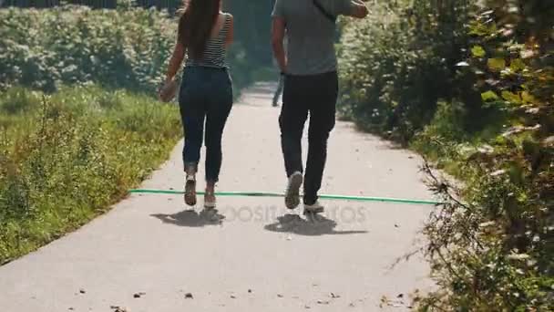 바람이 부는 날에 공원에서 아스팔트도로 따라 카메라에서 산책 하는 커플 — 비디오