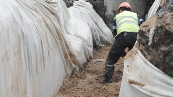 Αγία Πετρούπολη, Ρωσία - 26 Σεπτεμβρίου 2016: Εργαζόμενος στο σκληρό καπέλο σκάβοντας την άμμο με φτυάρι σε χαντάκι καλυμμένο με λευκό πανί — Αρχείο Βίντεο