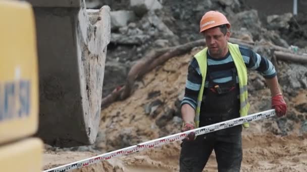SAINT PETERSBURG, RÚSSIA - SETEMBRO 26, 2016: Trabalhador de chapéu duro colocou régua industrial longa sob escavadeira no local de construção — Vídeo de Stock