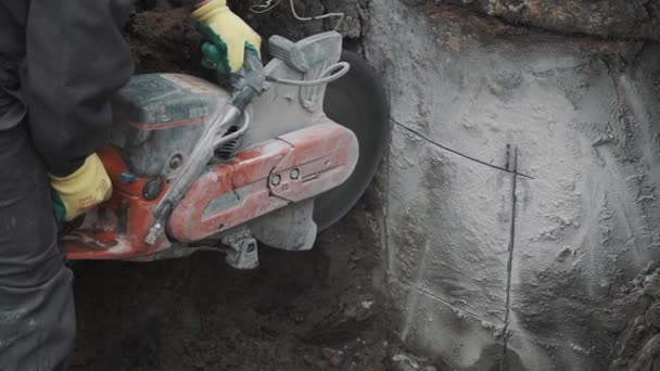 SAINT PETERSBURG, RUSSIA - SEPTEMBER 26, 2016: Worker with circular saw cutting concrete structure in trench at building site — Stock Video