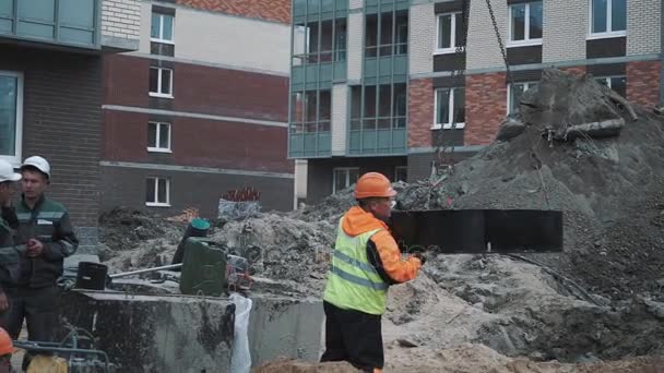 Sankt Petersburg, Ryssland - 26 September 2016: Arbetare i hård hatt spin betong manhål ring svängande på kedjor, bygga webbplats — Stockvideo