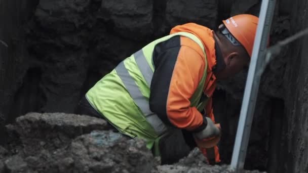 SAN PETERSBURG, RUSIA - 26 DE SEPTIEMBRE DE 2016: Trabajador con sombrero duro naranja excavando tierra en zanja con pala en obra — Vídeo de stock