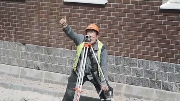 SAINT PETERSBURG, RUSSIA - 26 SETTEMBRE 2016: Costruttore con cappello rigido usa teodolite e tiene il pollice alzato in cantiere — Video Stock