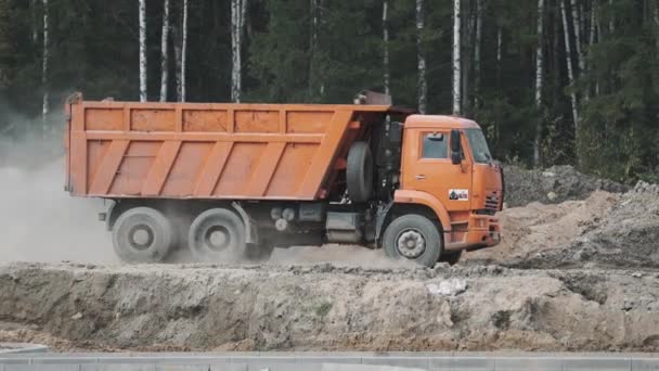 Sankt Petersburg, Ryssland - 26 September 2016: Orange builder truck ridning på smuts på byggnadsplatsen framför skogen — Stockvideo