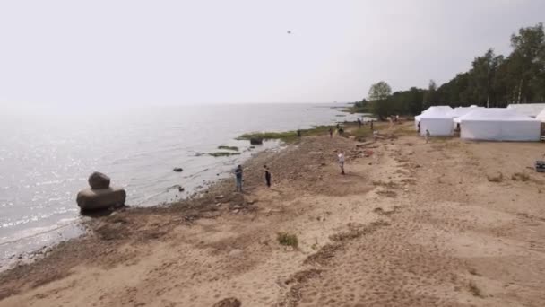 Sankt Petersburg, Ryssland - 30 juli 2016: Aerial skott människor flyga drakar på sandstranden havsstranden med vita tält sommartid — Stockvideo