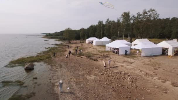 Sint-Petersburg, Rusland - 30 juli 2016: Luchtfoto mensen vliegers vliegen op zanderige kust met witte tenten in de zomer — Stockvideo