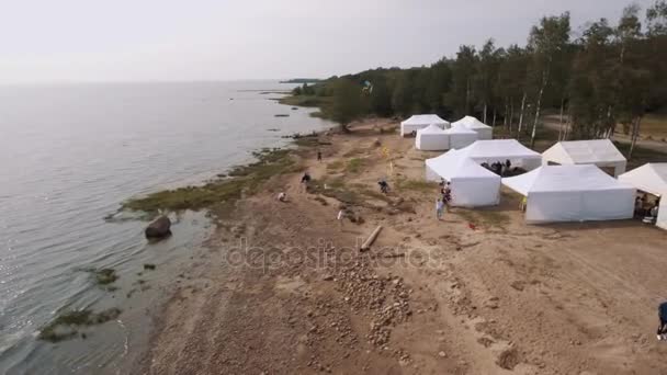 СЕНТ-ПЕТЕРБУРГ, РОССИЯ - 30 июля 2016 года: Люди с видом на небо запускают воздушных змеев на диком берегу моря с белыми палатками летом — стоковое видео