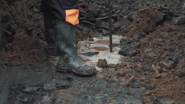 Homem em botas de borracha cutucando chão poça de terra com pedaço de armadura — Vídeo de Stock