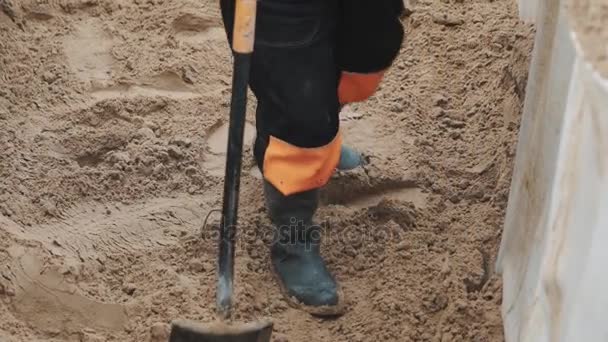 Tikje werknemer in rubberen laarzen met schop smoothing zand in sloot — Stockvideo