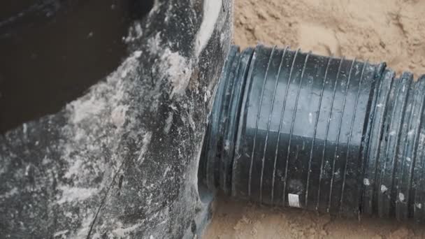 Sticking black ribbed plastic pipe in to round hole in concrete in sand ditch — Stock Video