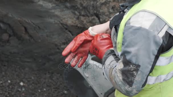 Працівник в канаві з циркулярною пилкою одягає червоні гумові рукавички. Сповільнення — стокове відео