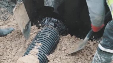 Kürek ve botlar ile kum siyah plastik boru çevresinde iki işçi sıkıştırmak