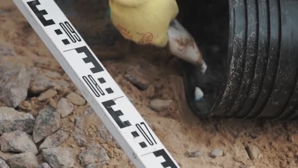 Worker in gloves put glue from tube on edge of black plastic pipe on sand — Stock Video